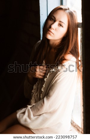 Beautiful brunette in blouse. Girl near window. Emotional portrait