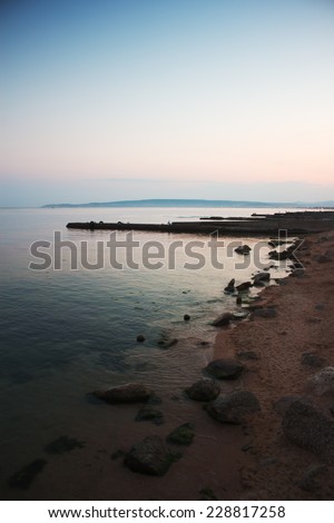 Seascape with breakwaters. Sea shore at sunset. Evening colors. Mountains on horizon