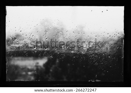 Rain drops on glass in frame. Texture of glass. Rainy weather. Sad autumn mood. Rural landscape outside window. Black and white photo