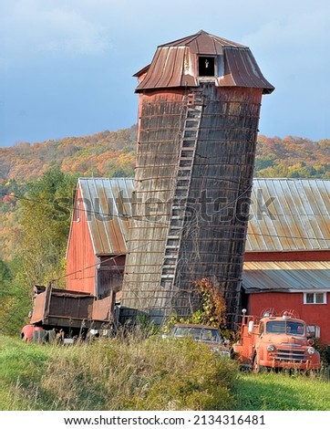 Amusing scene in rural Vermont with leaning hay silo, weathered red barn, and vintage fire engine. Heavy wire wrapped around silo and attached to old dump truck to keep tipsy silo from falling over. Foto d'archivio © 