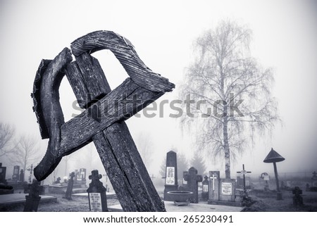Wood grave-cross with heart on it, cemetery and a tree in the background. Slight vignetting effect and toning applied, to enhance the mood.