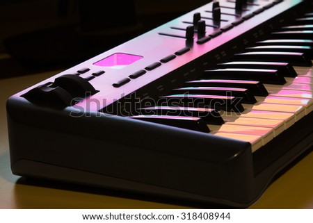 Deatil of a midi keyboard with modulation wheel, lit by a computer screen.