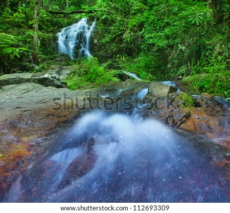 Mountain river in tropical rain forest in Thailand national park. Waterfall in jungle, green tropical plants and stones around.
