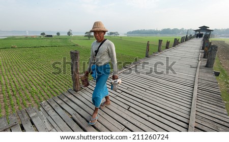 MANDALAY, MYANMAR - JAN 19, 2014: Unidentified male citizen of local village of Taungthaman lake crossing U Bein bridge - the longest wooden bridge in the world