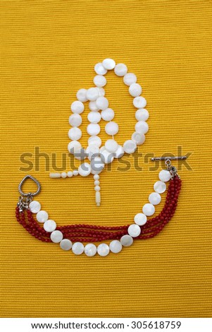 A sailboat image represented by a pearl necklace and a pearl-garnet bracelet on a yellow background