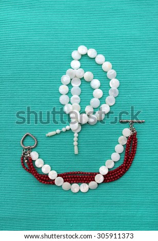 A sailboat image represented by a pearl necklace and a pearl-garnet bracelet on a blue background