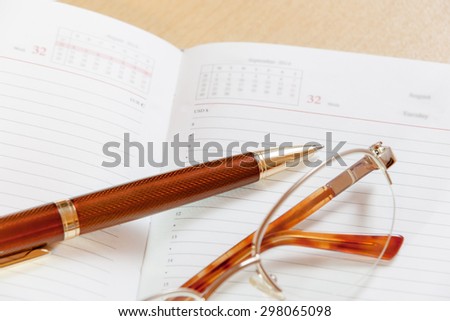Daily planner with glasses and pen on the table. Selective focus on pen