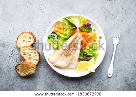 Fried fillet of sea white cod fish with juicy lettuce, capsicum, lemon, green peas on a large white dish on a gray background. Healthy balanced food. Top view Stockfoto © 