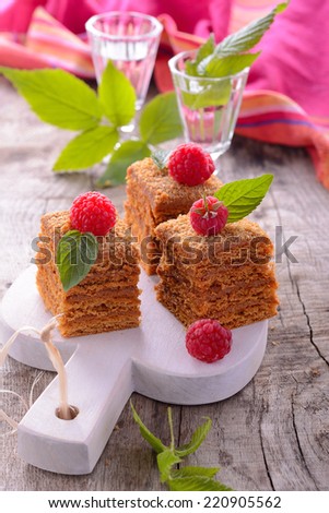 Slice of layered honey cake decorated with fresh raspberries raspberry mint leaves on the wooden background with a pink towel