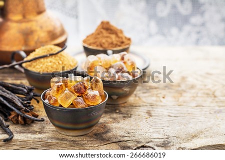 Crystals caramel brown sugar, natural vanilla pods, star anise, sugar cane, cocoa powder in old metal cup on a wooden background. selective Focus