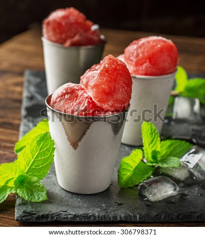 Frozen watermelon balls on a black stone plaque in portion cups with mint and ice. selective Focus
