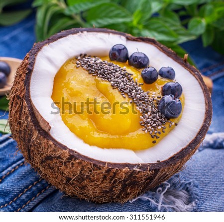 Breakfast mango and berry smoothies garnished with chia seeds and bee pollen in coconut on jeans background. Concept of healthy food. selective Focus