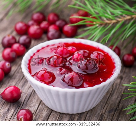 Fresh homemade cranberry sauce in portion bowl on dark wooden background with a scattering of ripe cranberries. selective Focus