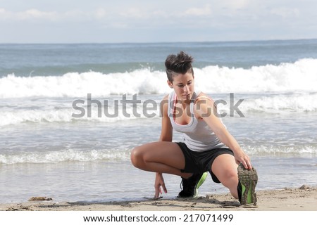 young woman with short hair doing lunges exercise on the beach on a sunny day