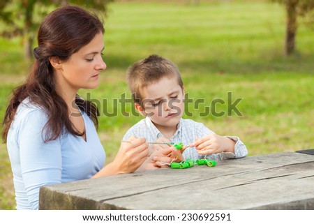 Young woman teacher teaches little young boy in white shirt painting with the brush to make  pasta beads
