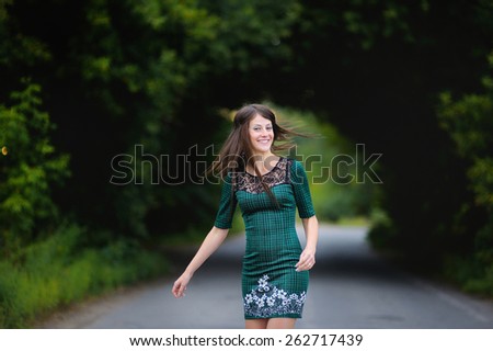 beautiful young girl, brunette with long straight Voros with beautiful breasts and long legs standing on the road against the background of green trees