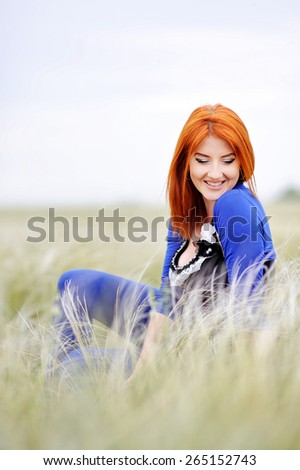 beautiful young girl with a beautiful figure, with long red hair and blue pants posing on the grass among flowers and green grass