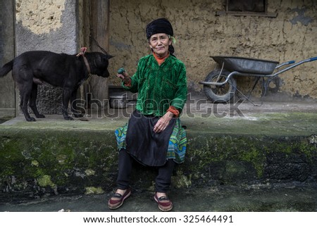 Hmong women sitting near black dog of her home . Hmong house in Ha Giang in Vietnam. An area adjacent to China. Ha Giang, Vietnam - September 19, 2015.