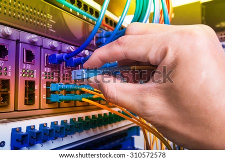 man working in network server room with fiber optic hub for digital communications and internet