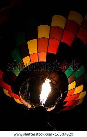 Color photograph of a colorful hot air balloon at night being lit up by fire.