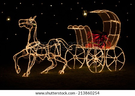 A large shining horse-drawn carriage stands in a meadow at night. Designed with golden Christmas Lights and a red shiny coachman bench.