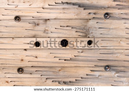 Pattern in the wood of the side wall of a large industrial cable reel consisting of grain, holes, metal parts and circular stapled metal brackets.