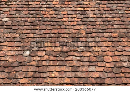 Detail shot of a roof area with very old roof tiles in various red brown shades. Partially overgrown with small round moss.
