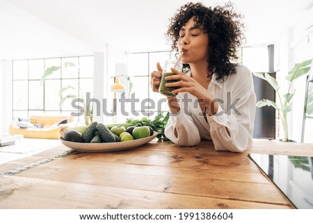 Young african american woman drinking green juice with reusable bamboo straw in loft apartment. Home concept. Healthy lifestyle concept. Copy space Foto d'archivio © 