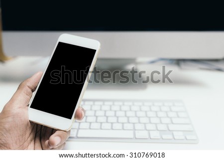 Hand to using smart phone in front of personal computer and keyboard