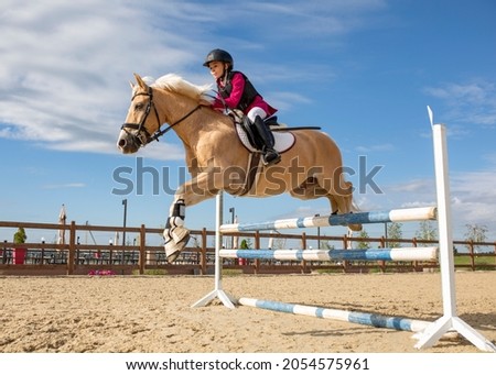A girl equestrian athlete jumps on a horse high barrier. Athlete in equestrian equipment, protective helmet. Vertical photo. Children's sports. Image with selective focus and noise effect, toning Сток-фото © 