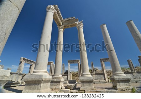 Remains of ancient greek columns and doorways together with intact entablature, against a clear blue sky. Image taken from the Agora at Perge.