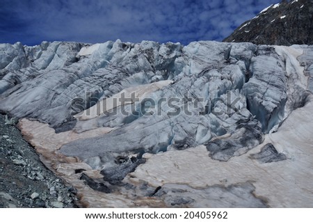 Ice cliffs on the edge of the Stockji glacier showing turquoise in the Swiss Alps. Sand blown in from the Sahara colours the old snow orange.