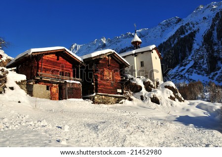 two old wood cabins and a chapel in the swiss alps with a layer of fresh snow