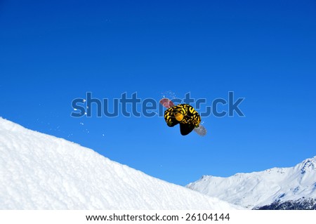 a snowboarder with black and yellow performing a spectacular jump trialing behind him the snow lifted by the jump.