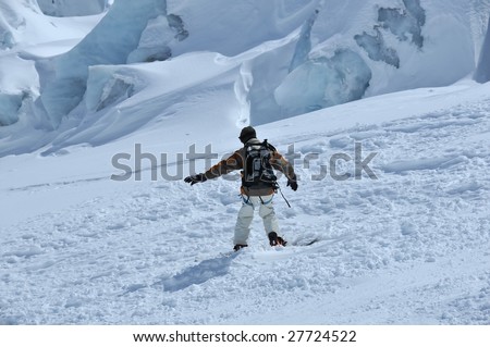 a snow-boarder descending an ice fall on a glacier. In the background blue ice blocks and crevasses.