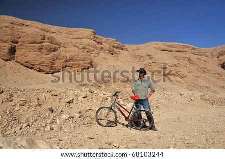Man with hat stands by an old fashioned bicycle in the desert