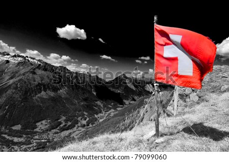 a swiss flag flutters from the top of a swiss mountain in the alps, above a valley with a swiss village, on a beautiful sunny day.