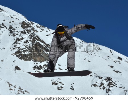 A free rider on snowboard performing a high grab in stripey black and white clothes, against a background of snow covered mountains
