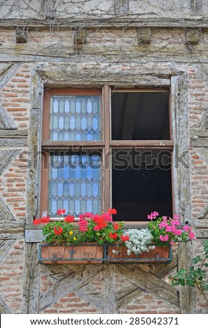 Window in traditional half timbered house decorated with a geranium filled window box, lead panel windows, and simple saltire and brick filled walls