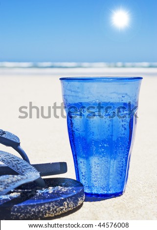 Blue glass with sparkling water and blue slip-slops on the beach