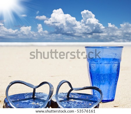 Beach shoes and a blue glass of sparkling water on a tropical island beach