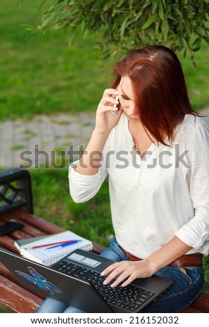 beautiful girl with a laptop in the park talking on the phone