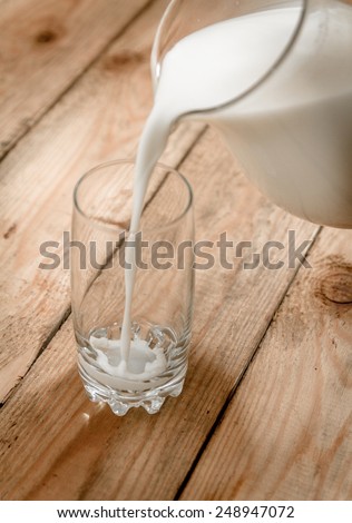Milk from a jug pouring into glass on old wooden table