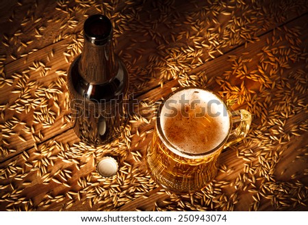 Bottle and glass of beer on old wooden table with grain. top view