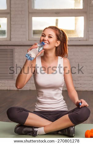 Beautiful athletic girl drinks water sitting on the mat. soft light