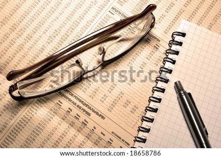 Glasses, pen and notebook laying on newspaper with financial numeric data. Warm (LBA) Photofilter.