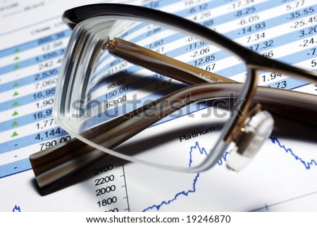 Glasses laying on printed financial report. Some graphs and data.