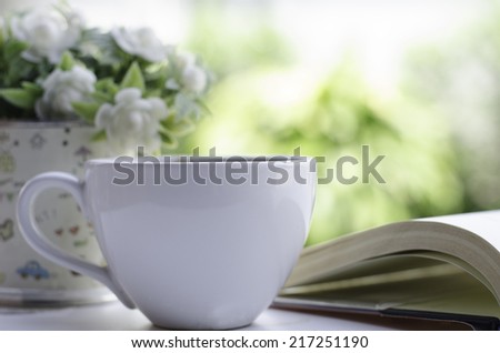White cup of coffee and open book garden background