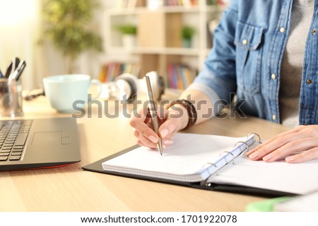Close up of student girl hand writing on notebook on a desk at home