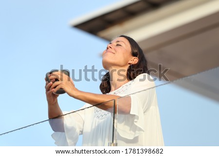 Satisfied adult woman with coffee cup breathing fresh air on a hotel balcony at summer Imagine de stoc © 